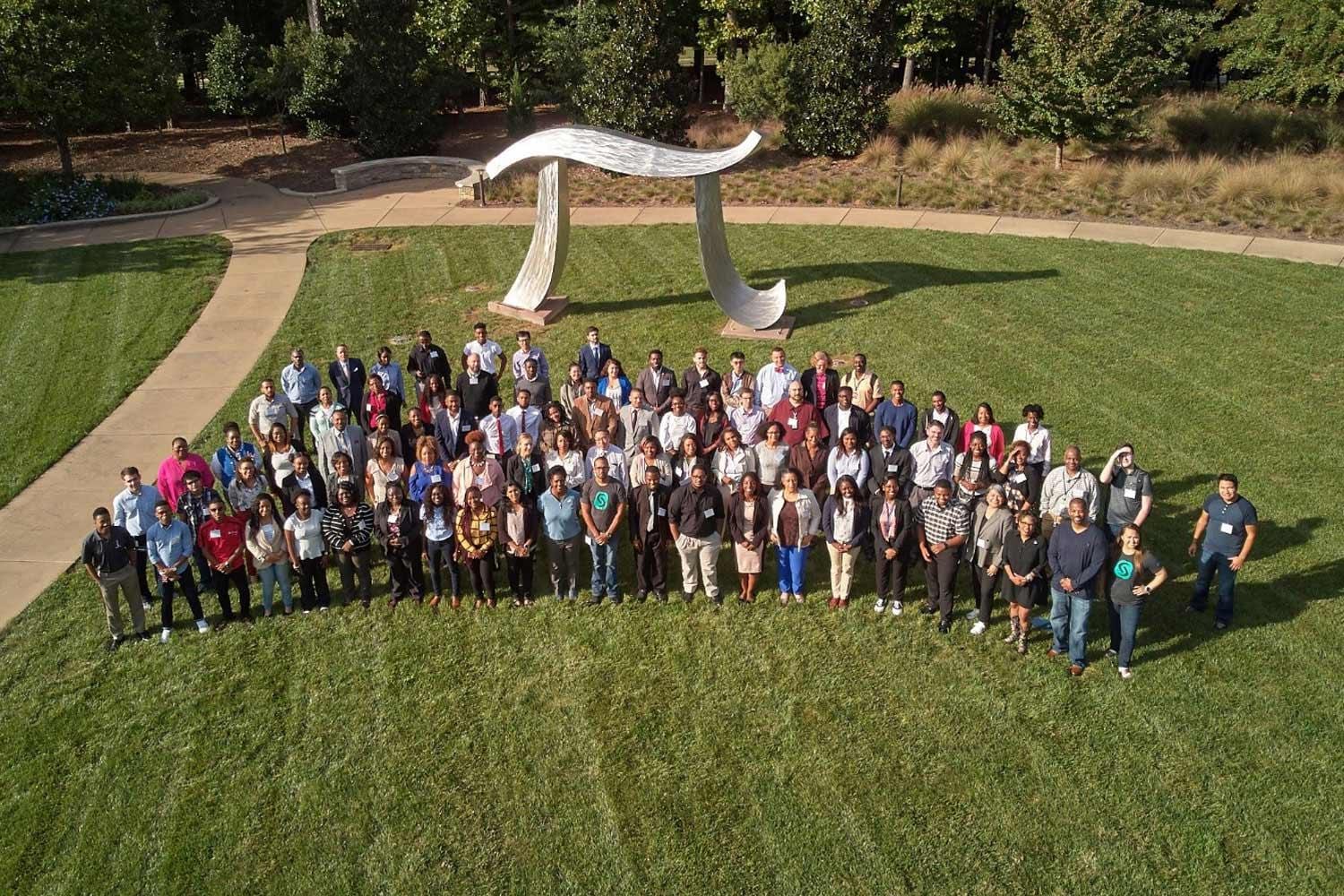 Group of SAS employees and interns on SAS headquarters lawn with large Pi sculpture behind them