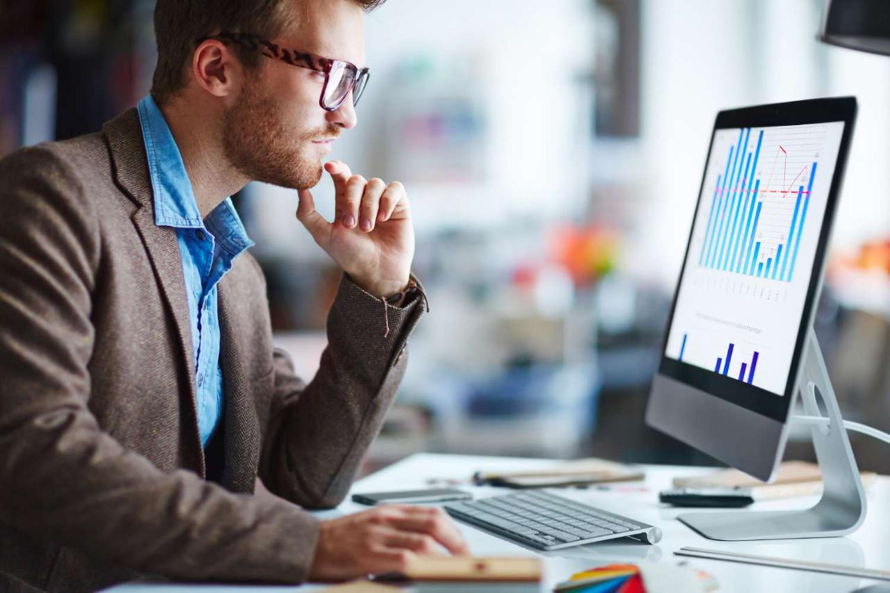 Looking at monitor -- male office worker looking at computer screen with data