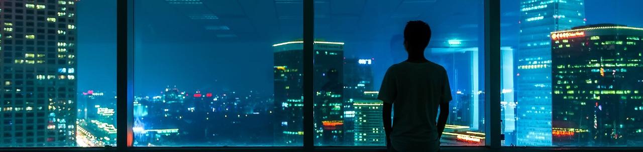 Man starring at city through window at night