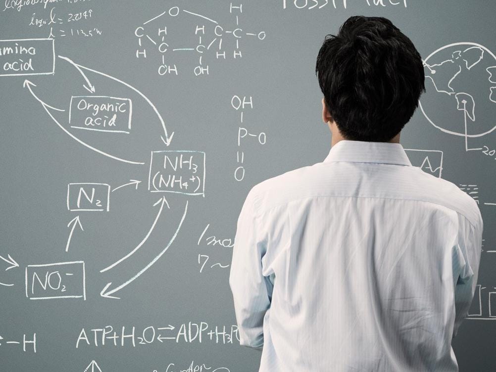 Man turned toward chalkboard solving equations