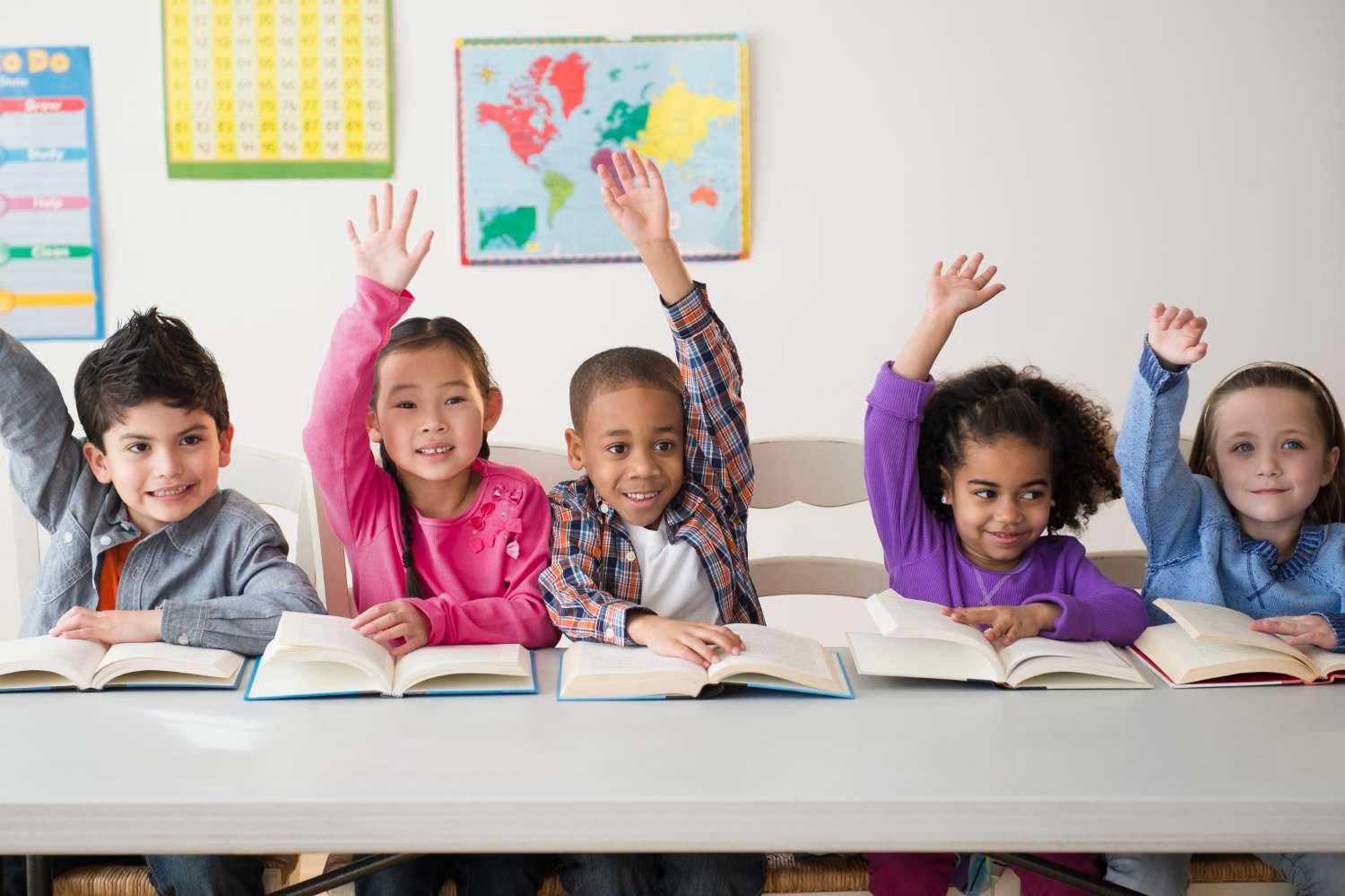Young students in classroom with books raising hands