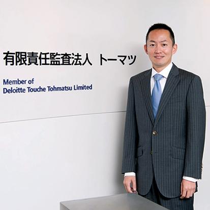 Asian business man standing inside in front of wall at Japan Tohmatsu Deloitte Touche building