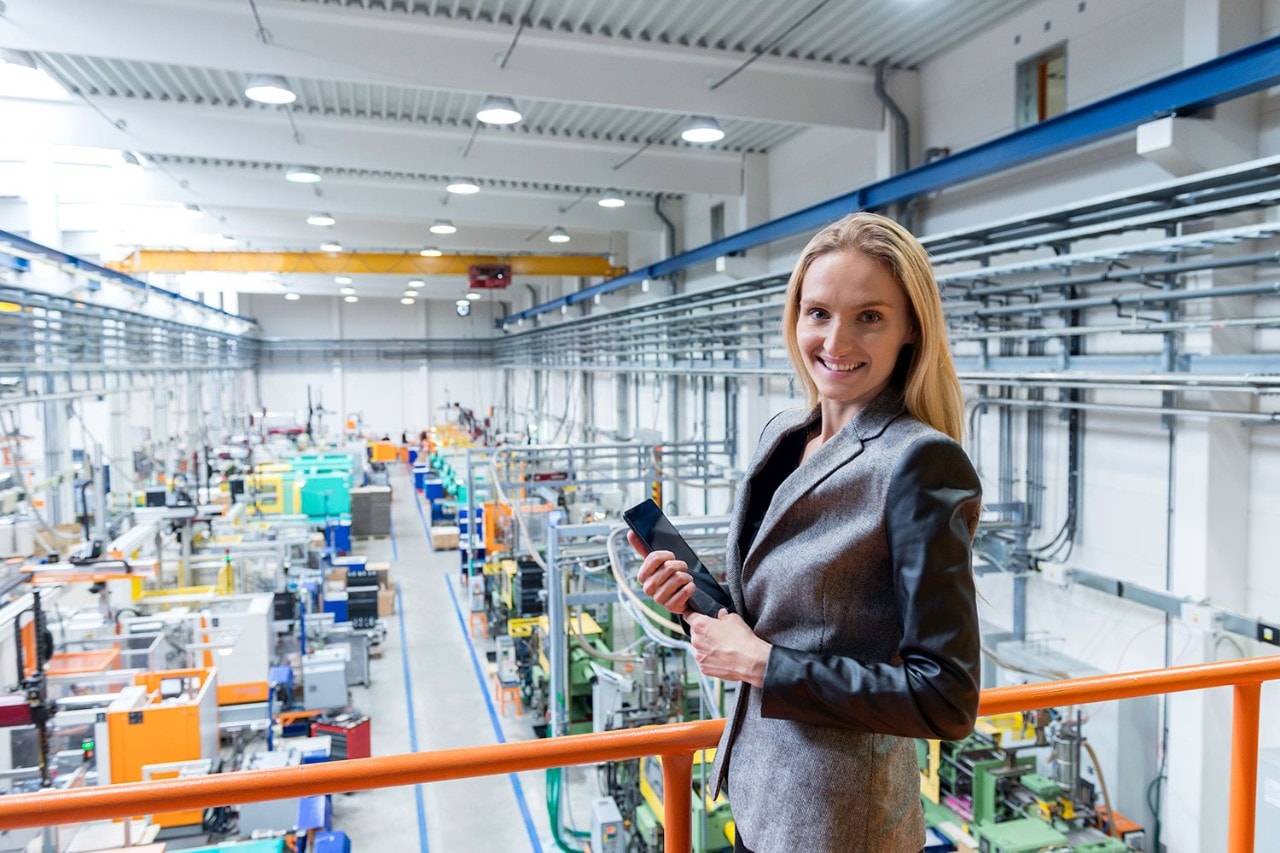 Business woman standing on balcony in factory and holding tablet