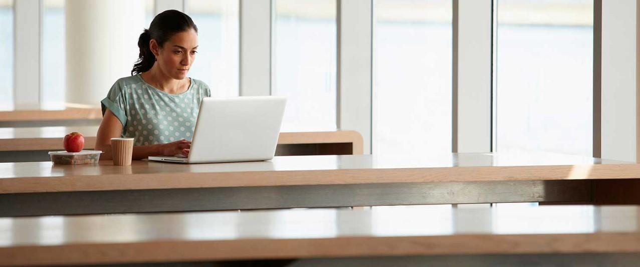 Woman using laptop with packed lunch on desk