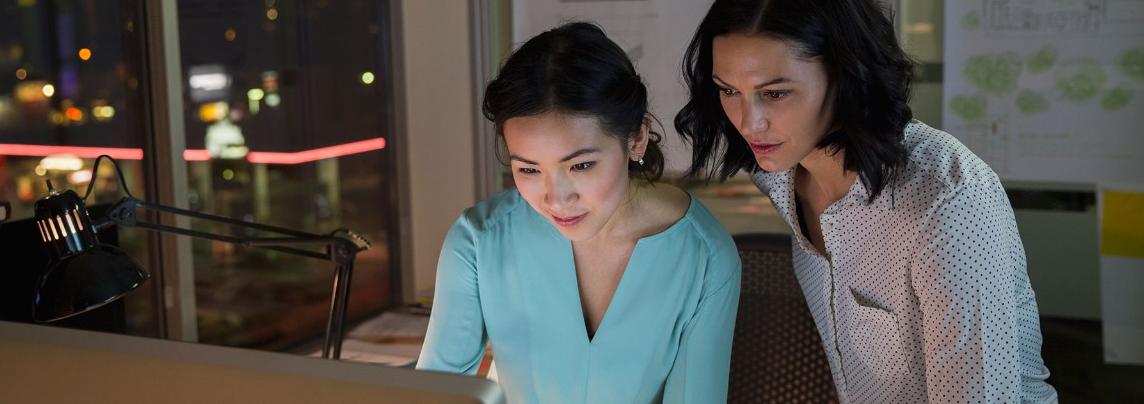 Two women looking at computer at desk at night