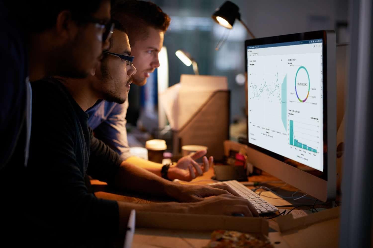 Group of young coworkers working with SAS® Visual Analytics in a dimly lit office