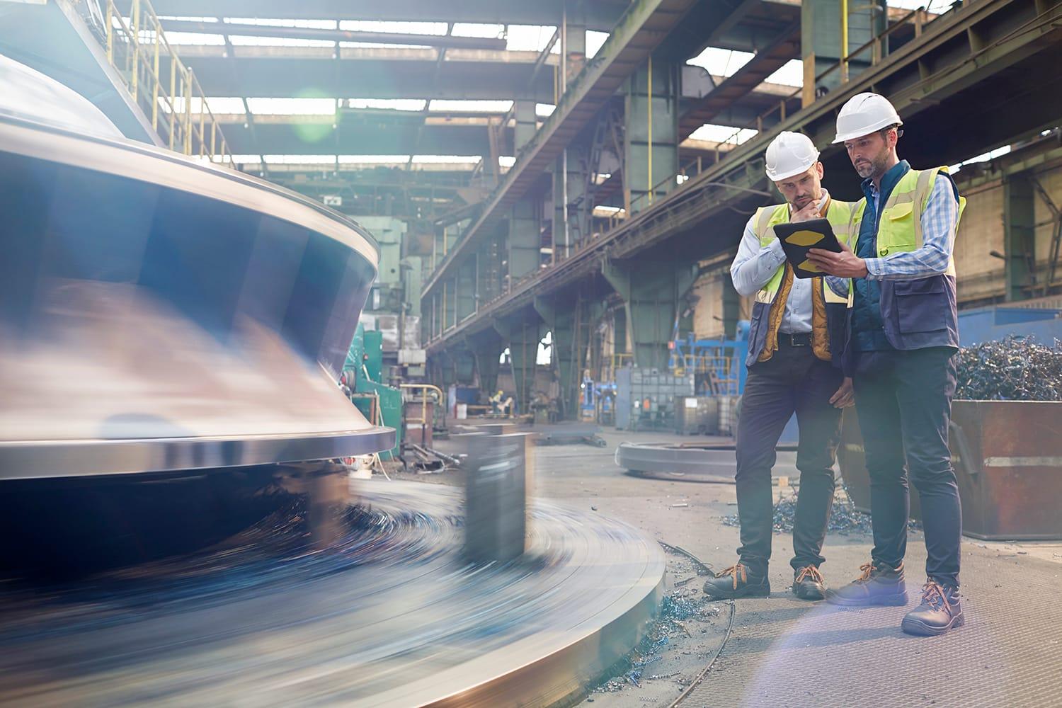 Two workers on factory floor with tablet device