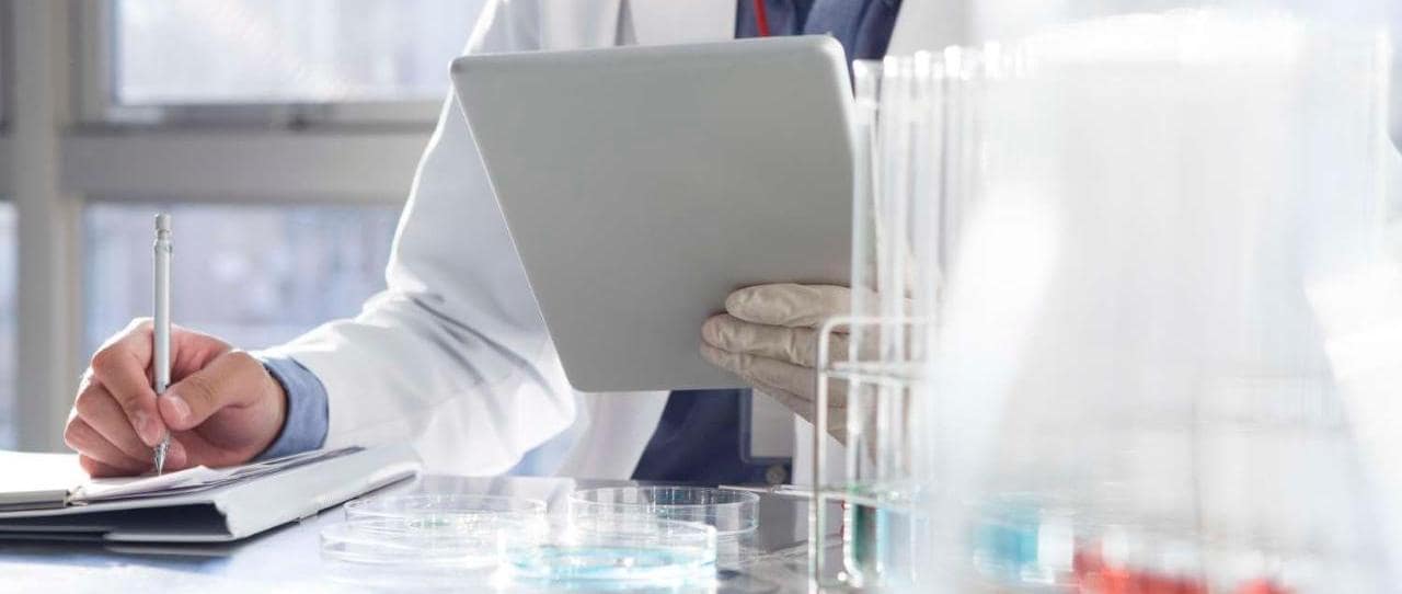 Scientist reading an electronic tablet while filling out a document