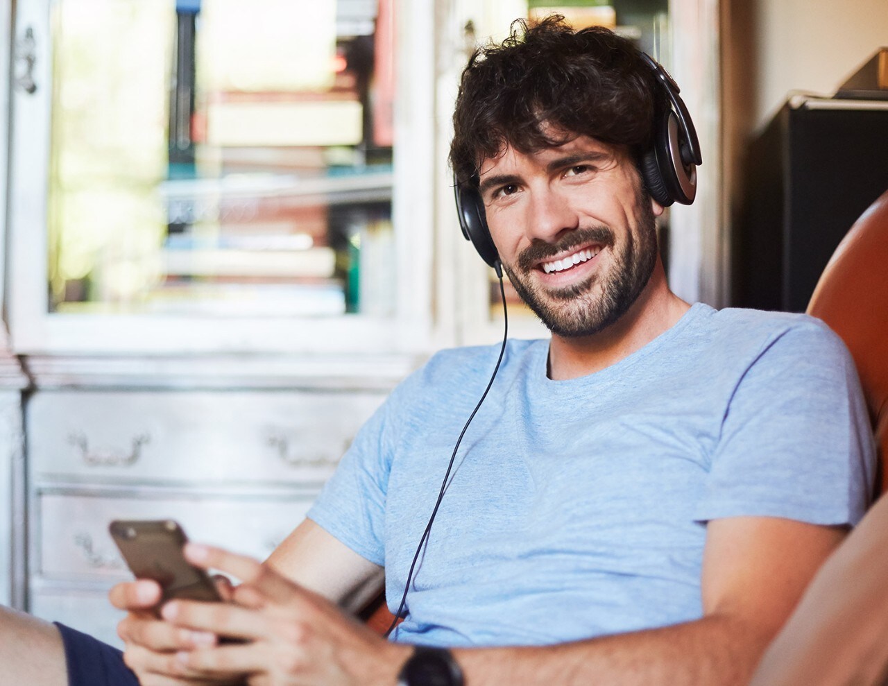 Man with beard wearing t-shirt holding phone with headphones