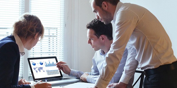 Two men and a woman looking at graphs and charts on a laptop