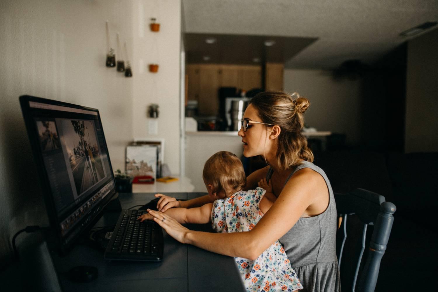 Young mother multitasking on computer with baby on lap