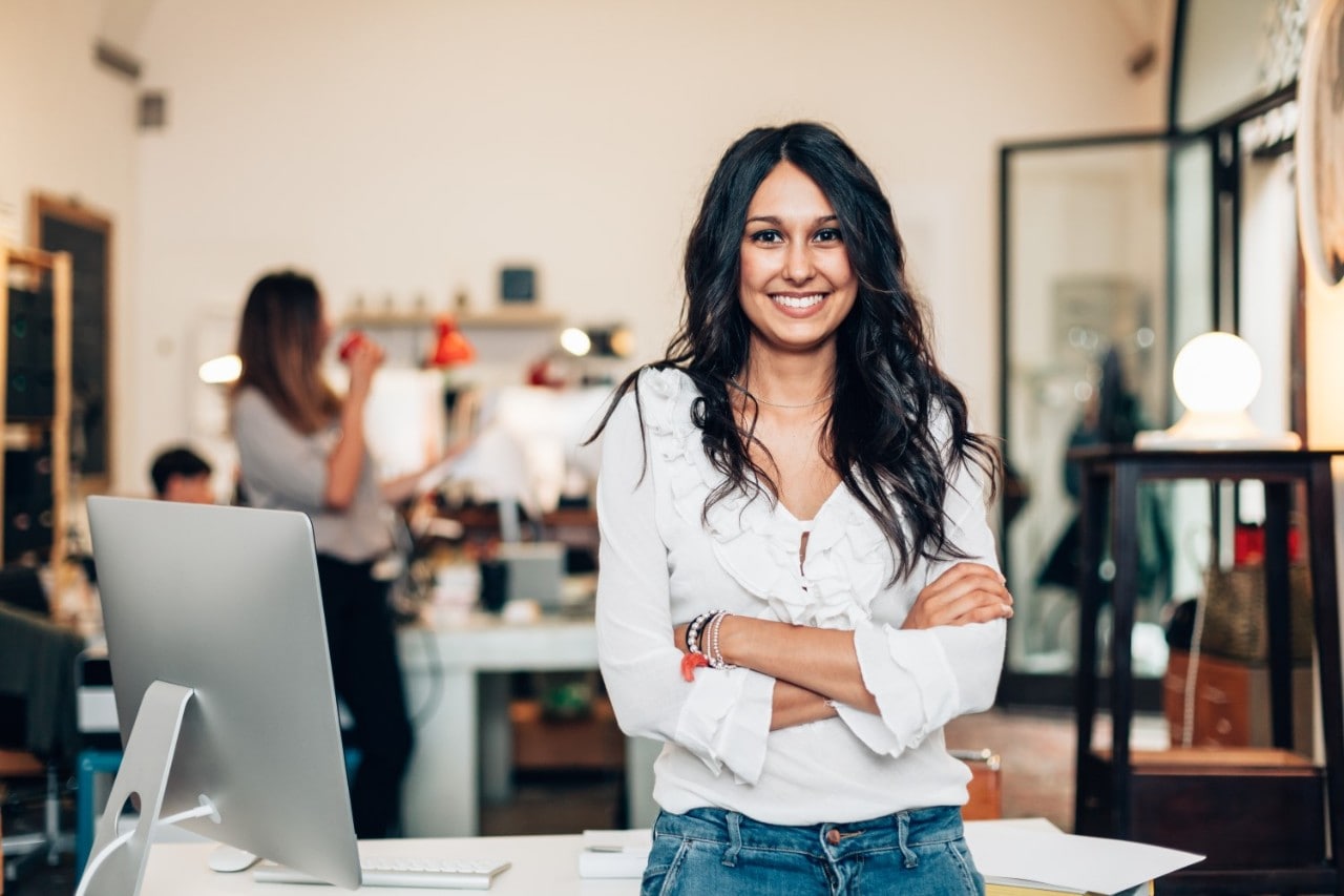 Woman Stand Up Smiling with Arms Crossed in Front of Work Desk