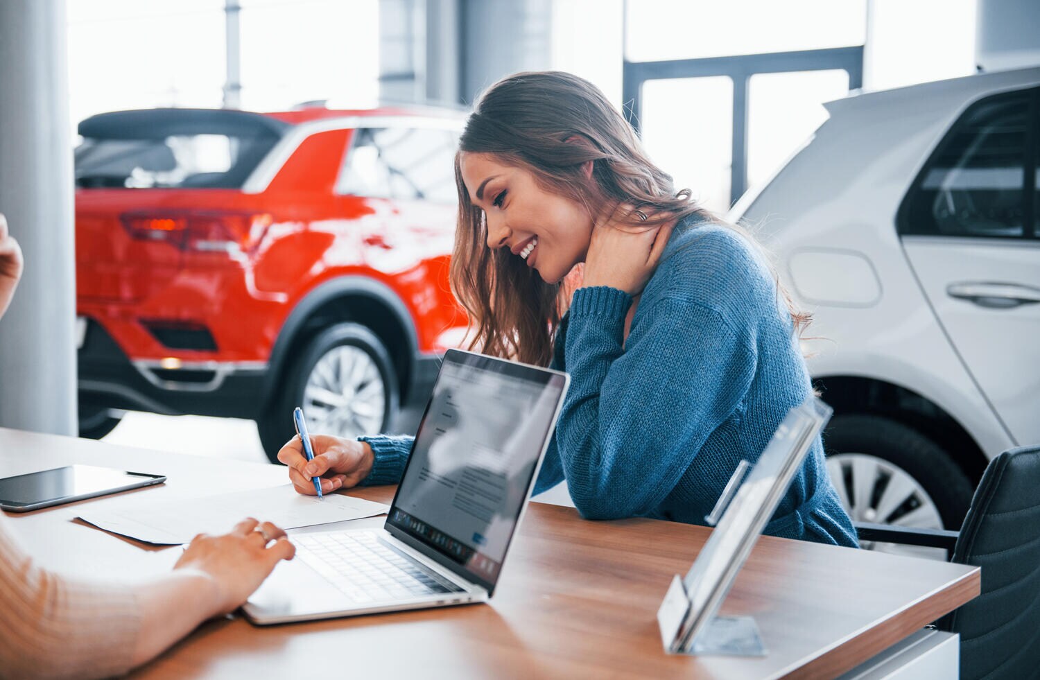 Cheerful woman sits with assistant in car shop and buying new vehicle