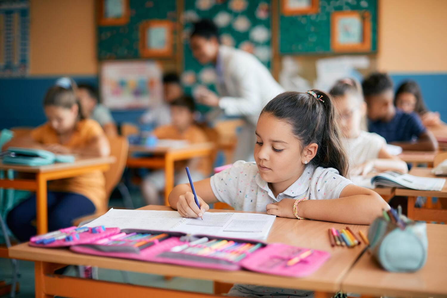 Young girl writing at desk in classroom