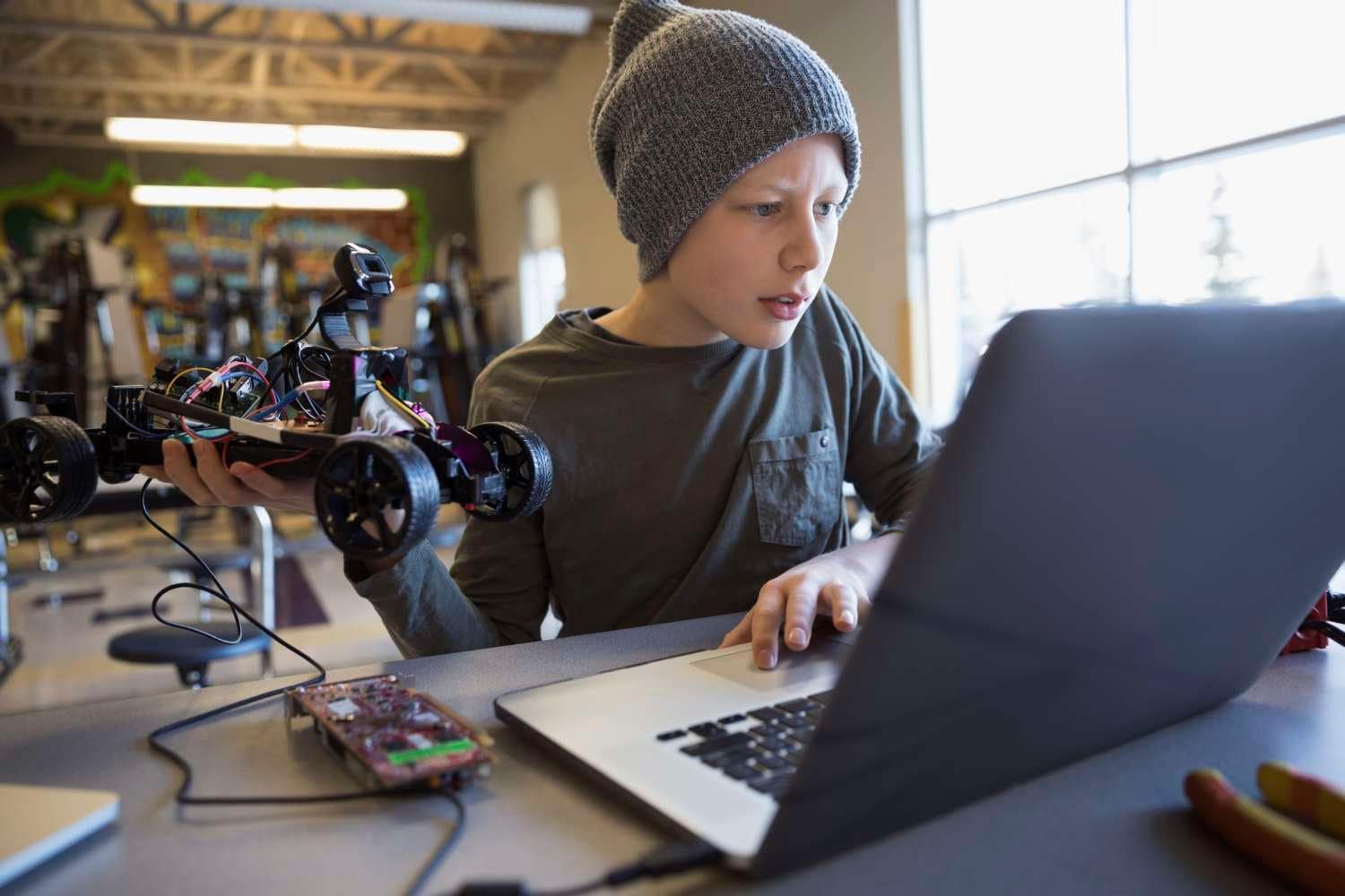 Young male student uses laptop to program remote control car