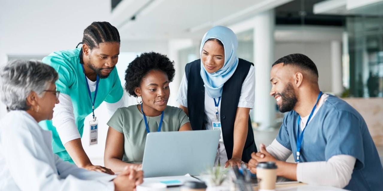 Diverse group of health care professionals gathered around laptop