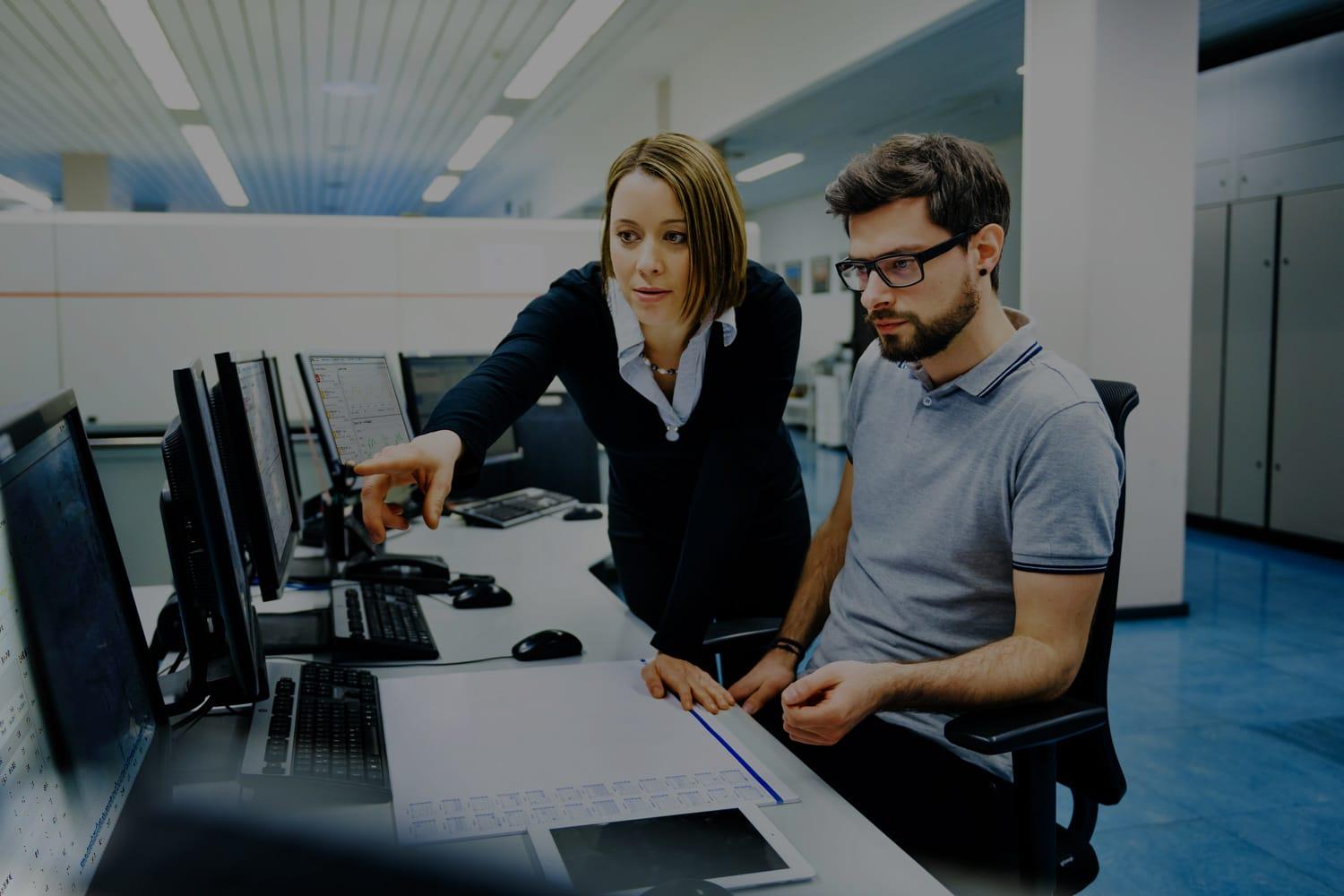 Two IT managers in command center study risk software Two IT managers in command center study risk software