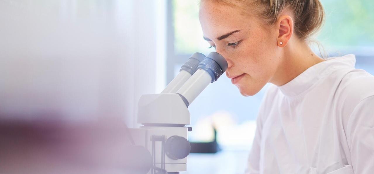 A female research scientist is analyzing a sample on her microsc