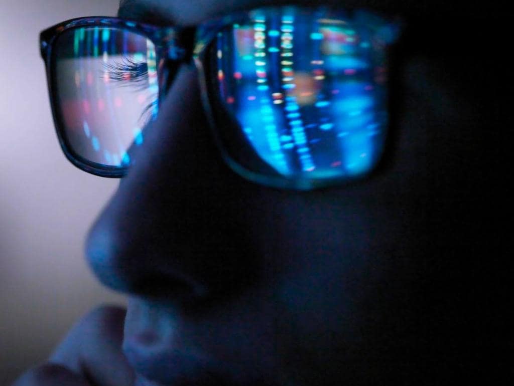 Computer screen reflection showing in criminal hackers glasses when browsing the dark web