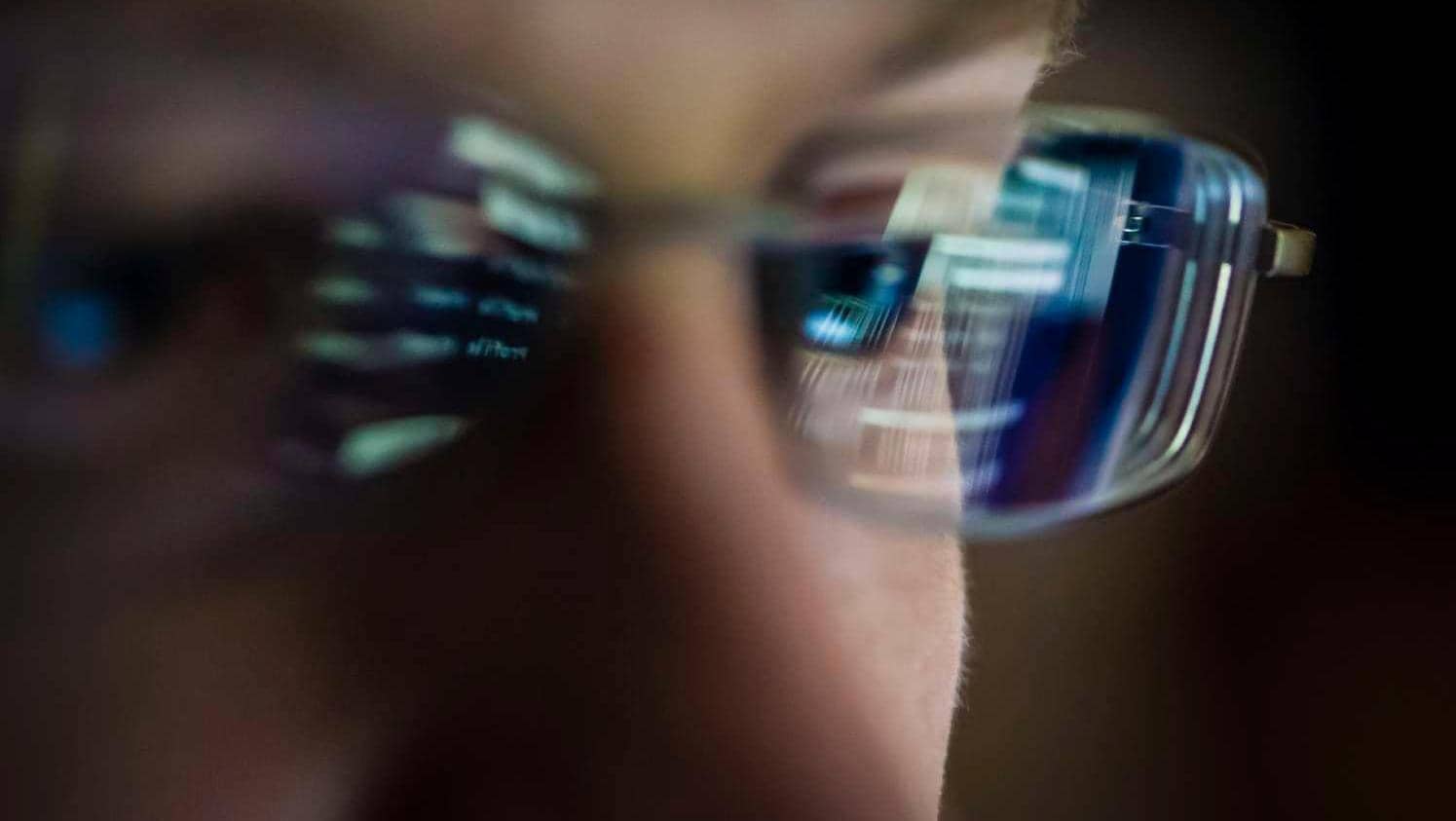 Close up of a person wearing glasses reflecting a screen