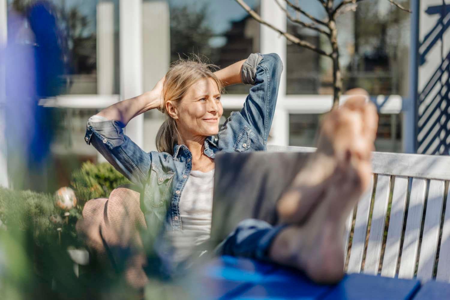 Smiling woman with laptop relaxing outside on garden bench