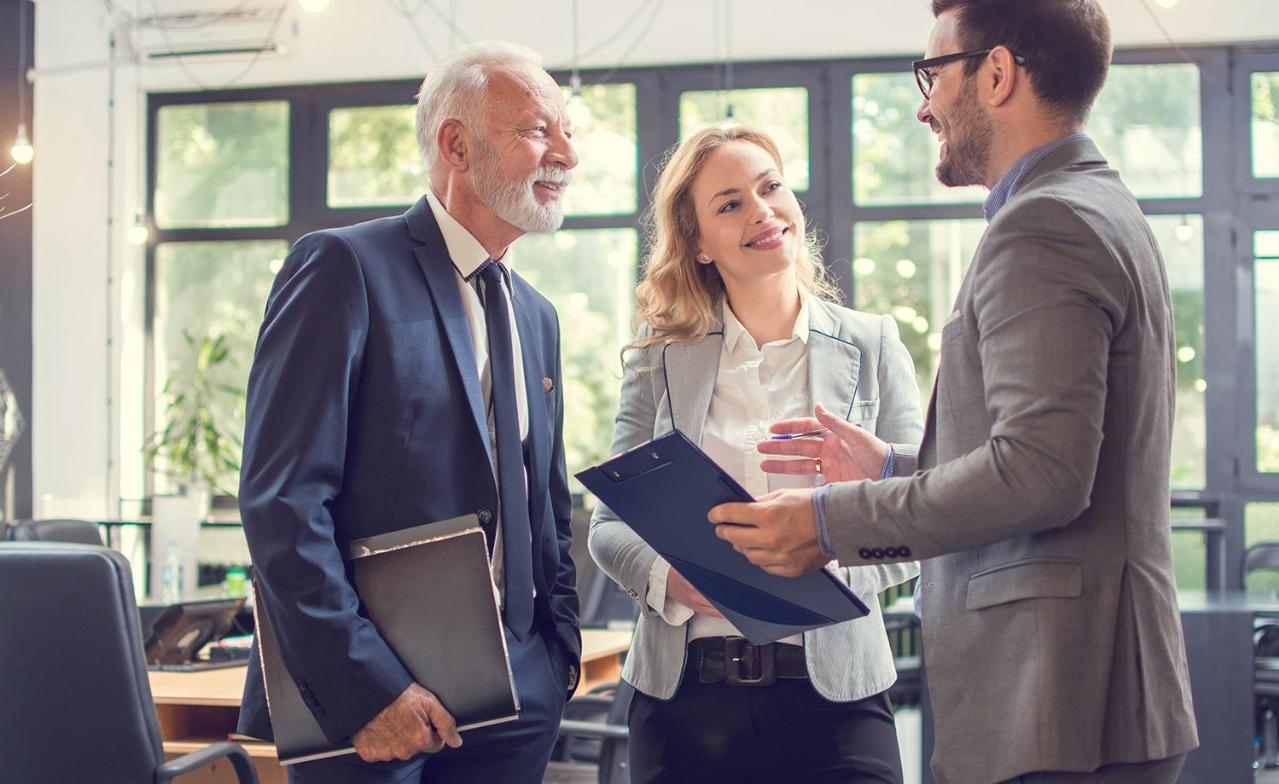 Two men and a woman standing and talking together in an office Two men and a woman standing and talking together in an office