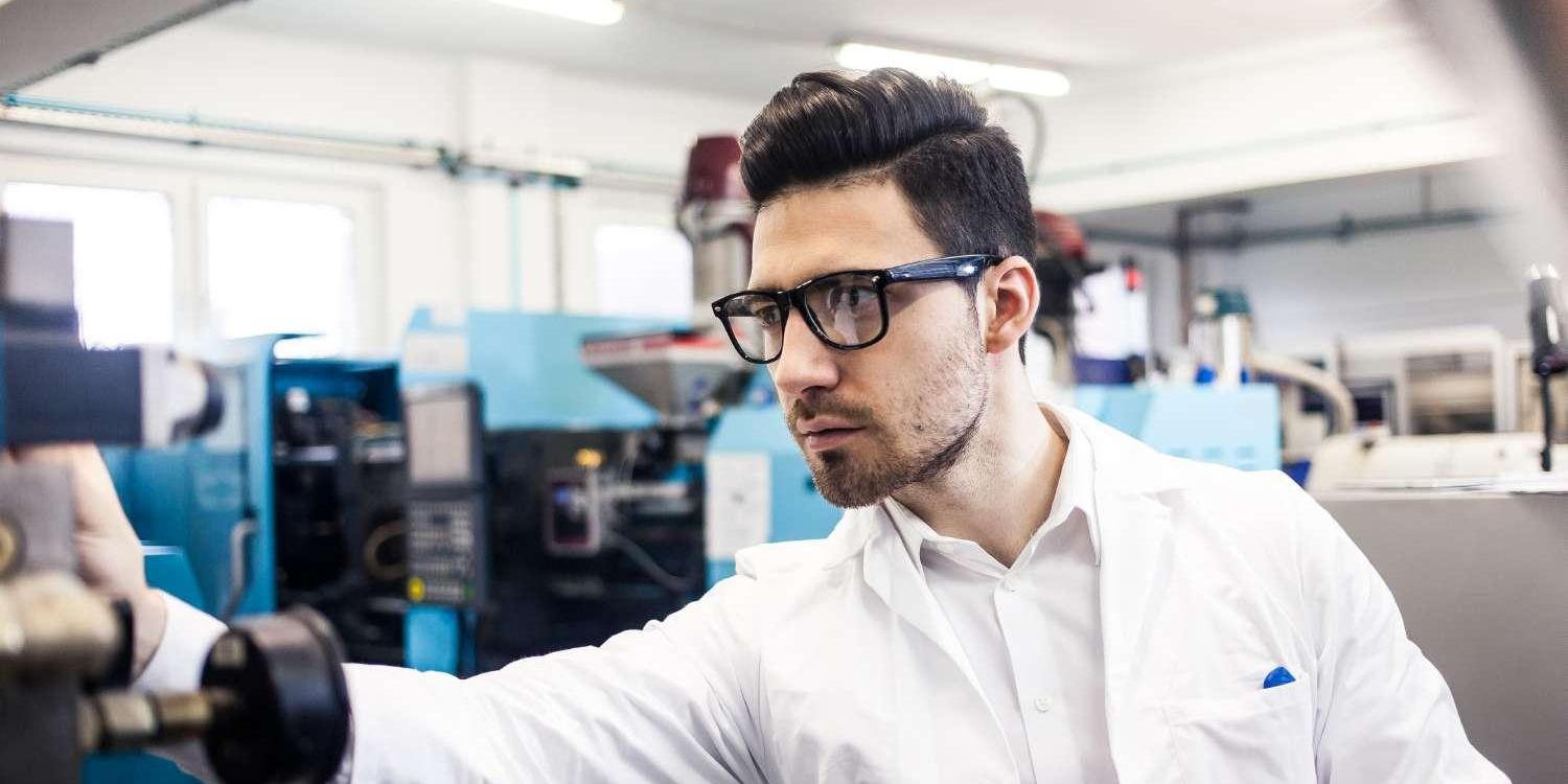 Male Engineer With Glasses and White Shirt Holding Tablet in Factory Workshop