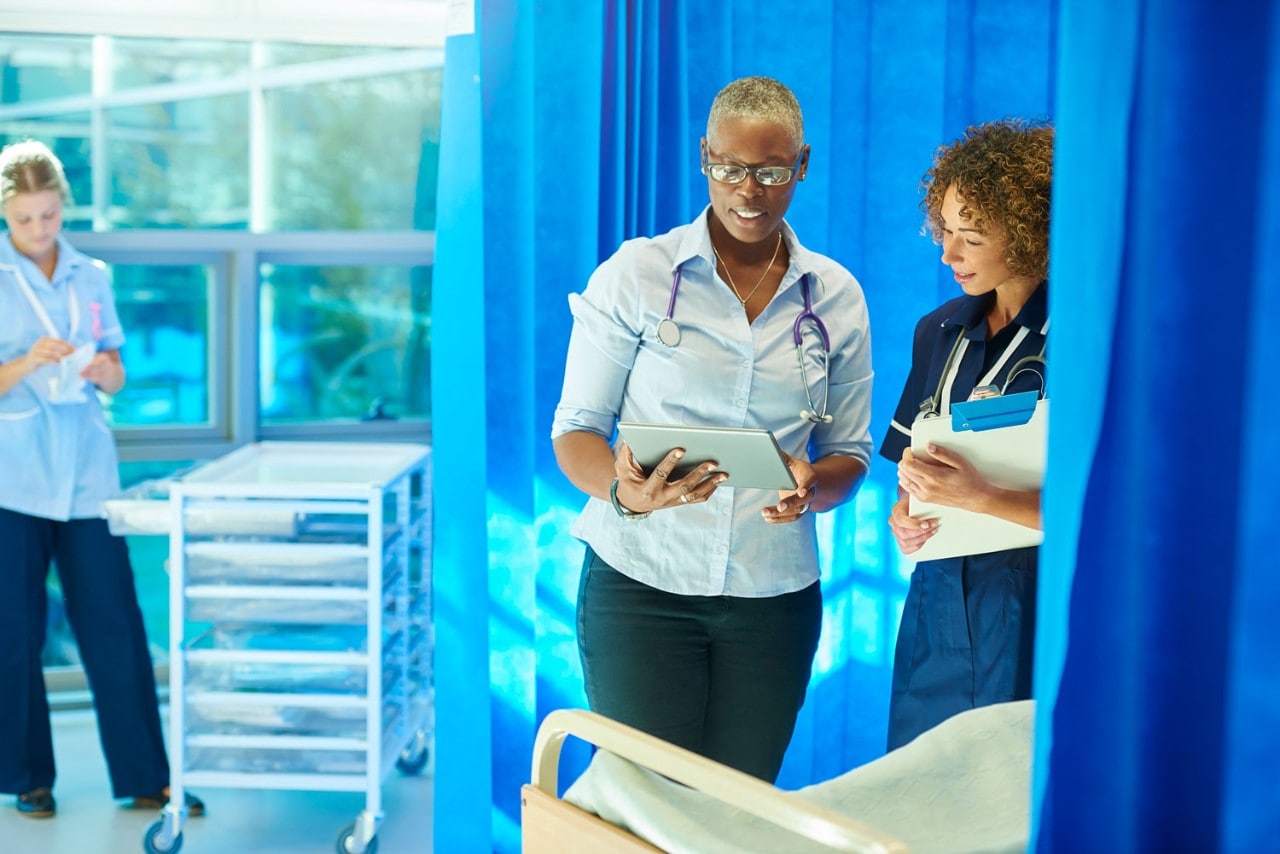 Female doctor is standing next to a hospital bed chatting to a nurse