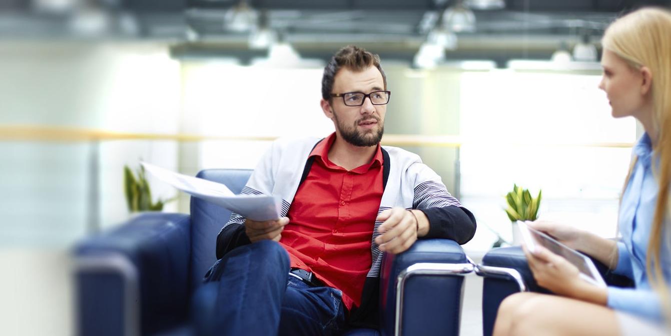 Man with report, woman with laptop, sitting discussing ideas