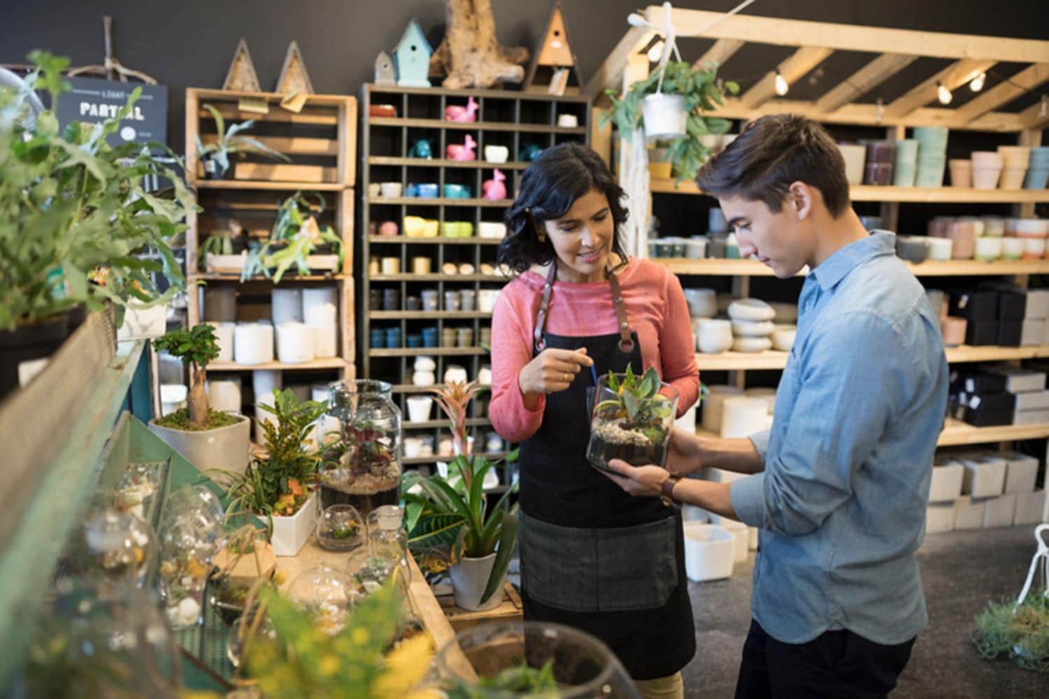 Female shop owner helping male customer shopping in plant shop 