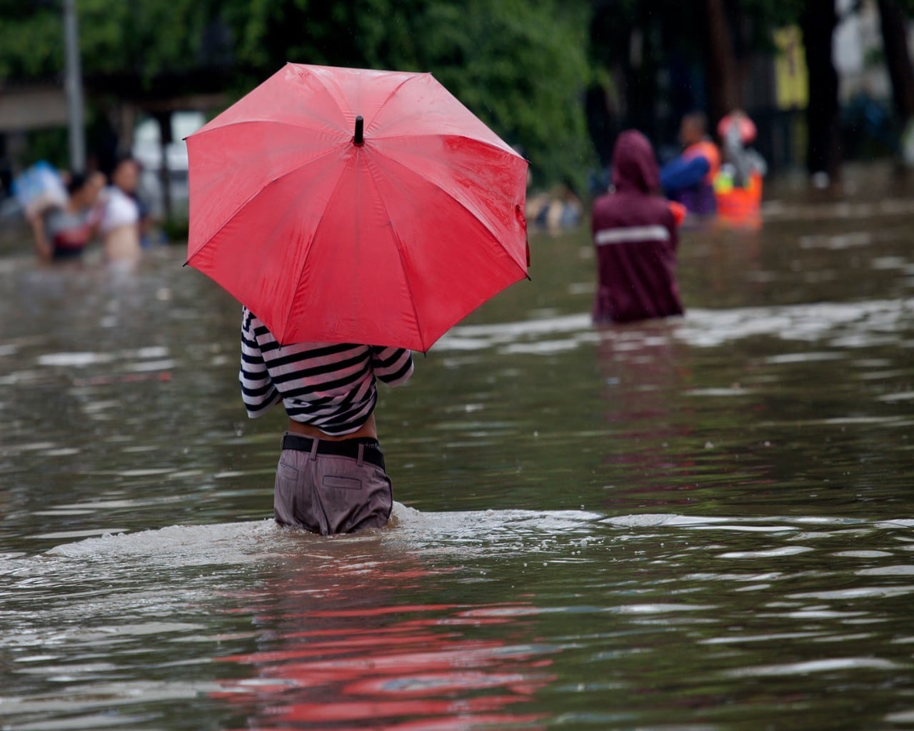 Man walks in waist-deep floodwater while holding a red umbrella.