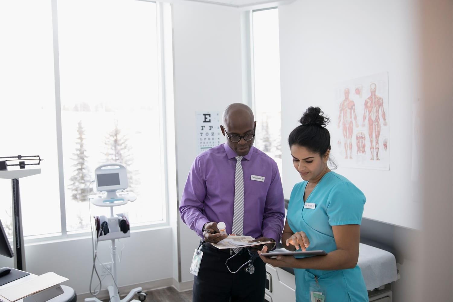 Male doctor with prescription medication and female nurse with digital tablet in clinic examination room  